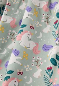 Kuvio, jossa on valkoisia yksisarvisia vaaleanpunaisilla ja purppuraisilla harjaksilla, valkoisia kaneja, joilla on sarvet, perhosia, kukkia ja kuunsirppejä vaalean vihreällä kankaalla.