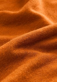 Tissu en tricot orange avec une texture douce, présentant un tissage fin et une légère brillance, affichant de doux plis et ondulations.