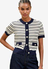 Cardigan a righe navy e crema a maniche corte con scollatura rotonda, bottoni color oro e due tasche frontali. Texture lavorata a maglia con dettagli a coste.