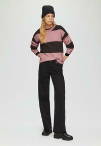 Gestreepte trui in roze en zwart, gebreid; relaxte pasvorm. Gepaarde met hoge zwarte jeans en stevige zwarte laarzen. Zwarte beanie gedragen.