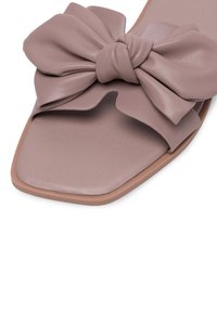 Odinių šlepečių sukamštymo švelniai mauviškai spalvos, kuriuose yra didelė palaidinė viršuje, kvadratinis batai ir minkštas tekstūruotas vidpadis su šviesiai ruda išorine dalimi.