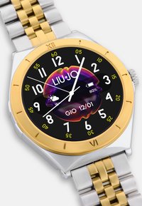 Liu Jo watch with a gold and silver stainless steel band, round gold bezel, black dial, bold white and yellow numbers, and colorful graphic detail.