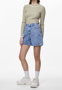Top de manga larga a rayas verdes combinado con unos pantalones cortos de mezclilla de tiro alto con bordados florales. Zapatillas blancas completan el conjunto.