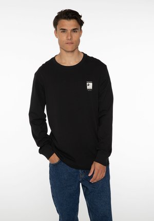 Sort langærmet T-shirt lavet af bomuld, med et lille hvidt logo på brystet, parret med blå denim jeans. Simpelt design og pasform.