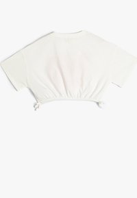 Camiseta blanca recortada con mangas cortas, dobladillo fruncido y lazos ajustables a cada lado. Hecha de una tela suave y ligera.