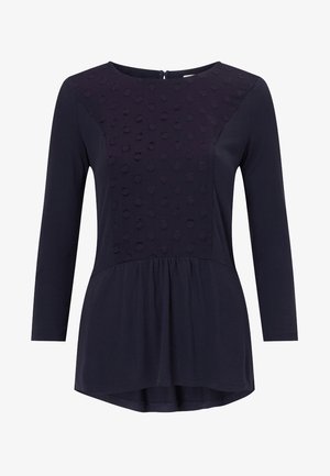 Granatowa bluzka z długim rękawem, z teksturowanym, kropkowanym wzorem na górnym panelu, lekkiego materiału, okrągłym dekoltem i falbaną u dołu.