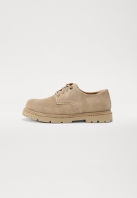 Beige mockasinsko med rund tå, snøredesign og lys gummisåle med synlig mønster for grep. Enkle sømdetaljer.