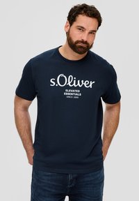 Jūrų mėlynos spalvos medvilnės marškinėliai su trumpomis rankovėmis, ant priekio esantis baltas atspaustas tekstas "s.Oliver Elevated Essentials Since 1969".