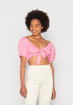 Top cropped rosa com mangas bufantes, apresentando um detalhe de laço na frente. Combinado com calças de cintura alta xadrez verde claro. Textura de tecido suave.