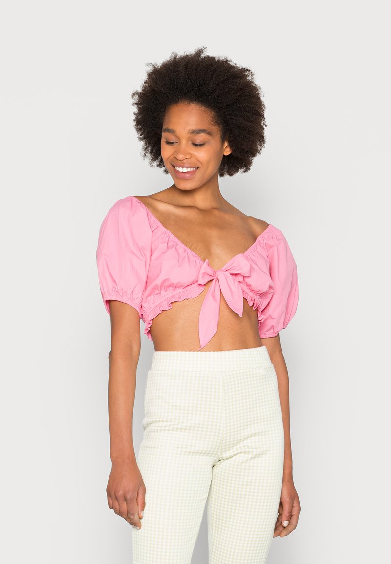 Top cropped rosa com mangas bufantes, apresentando um detalhe de laço na frente. Combinado com calças de cintura alta xadrez verde claro. Textura de tecido suave.