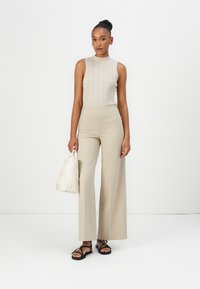 Beige ribbed knit tank top ja korkeavyötäröiset beige leveälahkeiset housut. Valkoinen laukku, jossa on geometrinen kuvio, mustat litteät sandaalit, joissa on hihnat.