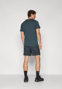Mænds mørk teal bomulds t-shirt parret med sorte mønstrede shorts, sorte sokker og sneakers. Enkel design med en afslappet pasform.