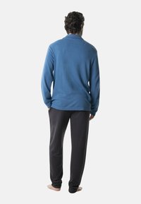Haut bleu à manches longues en tissu texturé, associé à un pantalon de pyjama gris foncé, vu de dos, sans chaussures.