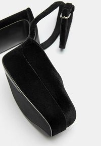 Musta samettinen platform-kengät, joissa on sileä, pyöreä muotoilu ja yhteensopiva säädettävä hihna. Varustettu kiiltävällä MUSTALLA pohjalla ja pehmeällä tekstuurilla.