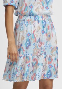 Jupe évasée en tissu bleu clair avec un motif abstrait coloré. Dotée d'une taille élastique et d'un ourlet à volants.