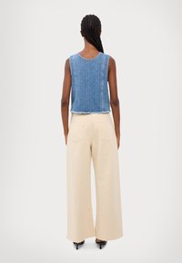 Top corto de mezclilla con dobladillo deshilachado, combinado con pantalones anchos beige. Ambas prendas tienen un corte relajado y texturas suaves.