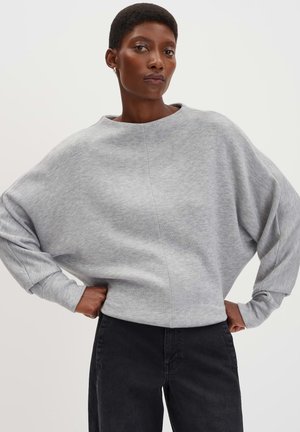 Grauer Sweatshirt mit weitem Boot-Ausschnitt, lässiger Passform und langen Ärmeln. Kombiniert mit schwarzen Jeans, die einen lässigen, bequemen Stil zeigen.