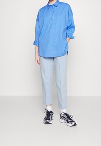 Světle modrá košile s knoflíky a texturovanými proužky, spárovaná se světle modrými zúženými kalhotami a černobílými sportovními botami.