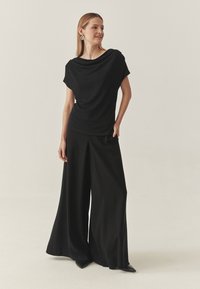 En sort draperet top parret med højtaljede sorte brede bukser. Glat stof med en elegant drapering. Spidse sorte sko fuldender looket.