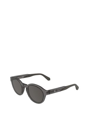 Lunettes de soleil rondes noires Calvin Klein avec des verres foncés et des montures noires translucides montrées en angle.