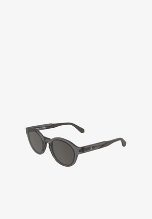 Runde schwarze Calvin Klein Sonnenbrille mit dunklen Gläsern und durchscheinend schwarzen Rahmen, aus einem Winkel gezeigt.