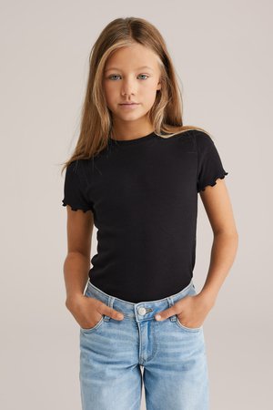Tricou negru cu dungi, cu mâneci scurte și ondulate, asortat cu blugi de denim albaștri deschiși. Accent pe textura elegantă și potrivirea lejeră.