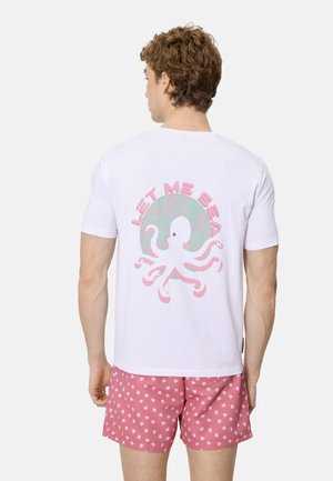Hombre vistiendo una camiseta blanca con un pulpo rosa y el texto "LET ME SEA" en la espalda, combinado con pantalones cortos rosas con un estampado de pulpos blancos.