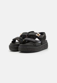 Sandali platform neri con cinturini intrecciati e fibbie dorate. Presentano suole testurizzate per la presa e solette imbottite per il comfort.