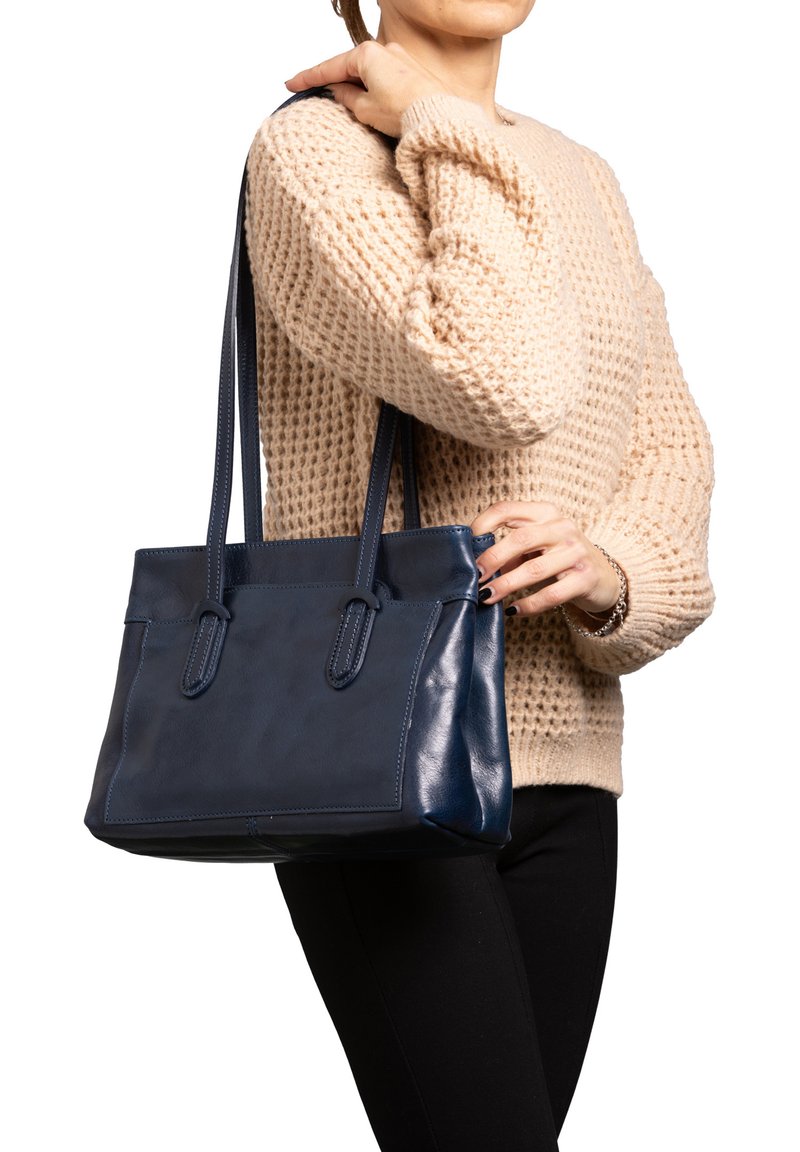 Sac fourre-tout en cuir bleu marine avec deux longues poignées, texture lisse, forme rectangulaire et détails de couture subtils sur les côtés.