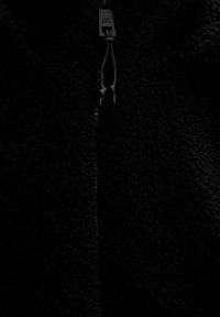 Black fleece zip-up jacket with a soft, textured surface; features a central zipper and pull-strings. No distinct patterns or accents.