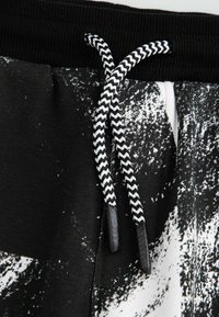 Czarno-białe dresy z teksturowanym abstrakcyjnym wzorem, charakteryzujące się grubym pasem i plecionym sznurkiem do regulacji z czarnymi końcówkami.