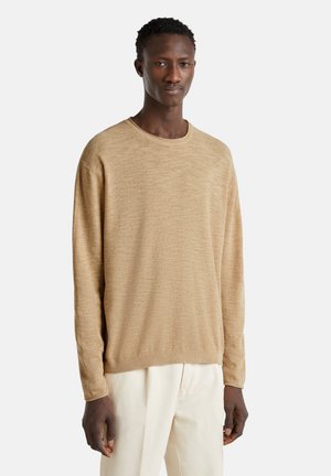 Suéter de punto beige con cuello redondo, mangas largas y una tela texturizada; combinado con pantalones de color claro.