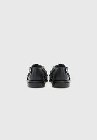 Black leather shoes with low profile, textured detailing, and decorative accents on the sides. Flat soles and round toe design.