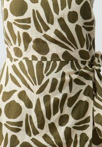 Abstract olijfgroene vormen op off-white stof met een strikdetail rond de taille van een kledingstuk.