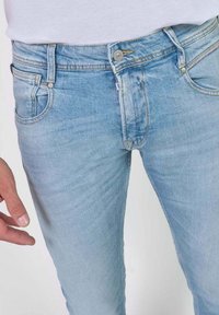 Vaqueros de mezclilla azul claro con un diseño ajustado, estilo clásico de cinco bolsillos y un ligero desgaste para textura y detalle.