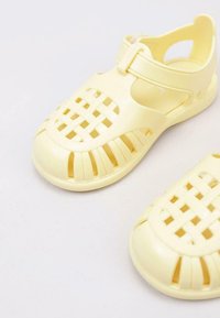 Yellow plastic sandals with a woven design, open sides, and a buckled strap. Each shoe features a rounded toe and textured sole.