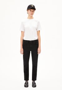 Svarta jeans med rak passform, ihop med en vit t-shirt. En svart keps med en gul sol-design fulländar looken, bärs tillsammans med svarta skor.