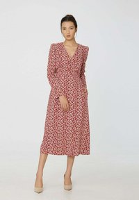 Robe midi florale rouge avec un décolleté en V, des manches longues et des poches. Fabriquée en tissu léger, elle présente un imprimé botanique délicat blanc.