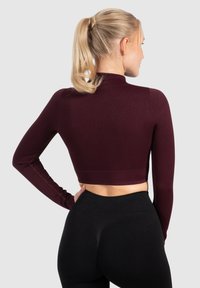 Burgundowy, prążkowany crop top z długim rękawem i stojącym kołnierzem. Połącz z czarnymi legginsami o wysokim stanie, podkreślającymi dopasowaną sylwetkę.