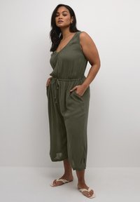 Olive green jumpsuit in lightweight fabric, sleeveless design, with a v-neck, drawstring waist, and side pockets; relaxed fit crop legs.