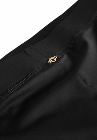 Sort stofbånd med syede sømme. Har en guldfarvet logoaccentside, der fremhæver materialets glatte tekstur.