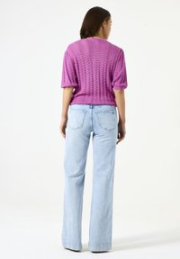 Paarse gebreide top met korte mouwen en een open weefpatroon, gecombineerd met lichtblauwe high-waisted flared jeans met achterzakken.