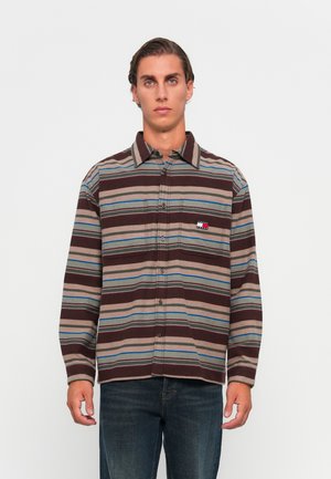 Striped button-up shirt featuring brown, blue, and green colors; made of textured fabric with a pocket and logo detail on the chest.