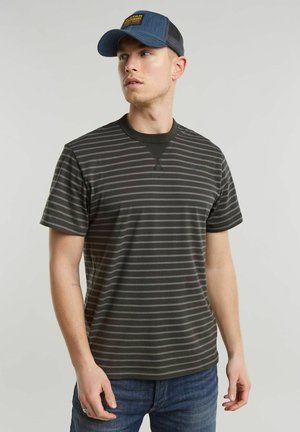 T-shirt a righe nere con scollatura rotonda e maniche corte, realizzato in tessuto morbido. Indossato con un berretto blu e jeans di denim.