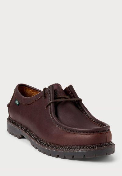 Zapatos de piel marrón con punta redondeada, detalles cosidos y suela de goma. Presentan un diseño de cordones y una etiqueta de marca sutil.