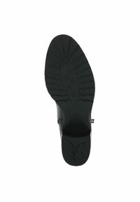 Suela de zapato negra con un patrón de trádeo texturizado, que presenta un logo de mariposa y un diseño de tacón plano. El material parece duradero y flexible.