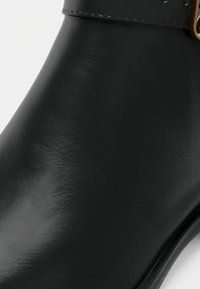 Bottine en cuir noir avec une texture lisse et des coutures visibles près du bord supérieur.