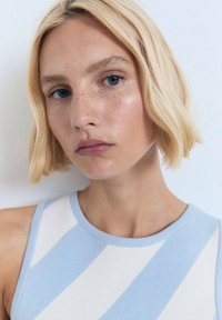 Sleeveless knit top featuring blue and white stripes, a round neckline, and ribbed texture. Model has short blonde hair and freckles.
