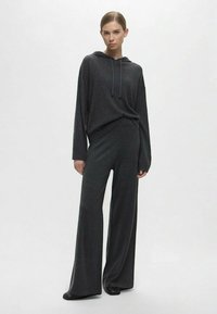 Felpa con cappuccio in maglia grigio scuro, con coulisse, abbinata a pantaloni a gamba larga; entrambi presentano una consistenza morbida e una vestibilità rilassata.