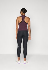 Maroon ribbed tank top with high neck and black racerback, paired with black leggings, showcasing a fitted design and minimalistic logo detail.